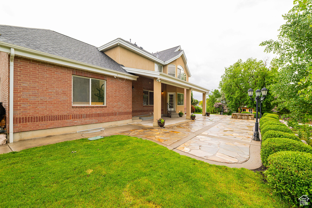 Back of property featuring brick siding, a patio area, a lawn, and a shingled roof