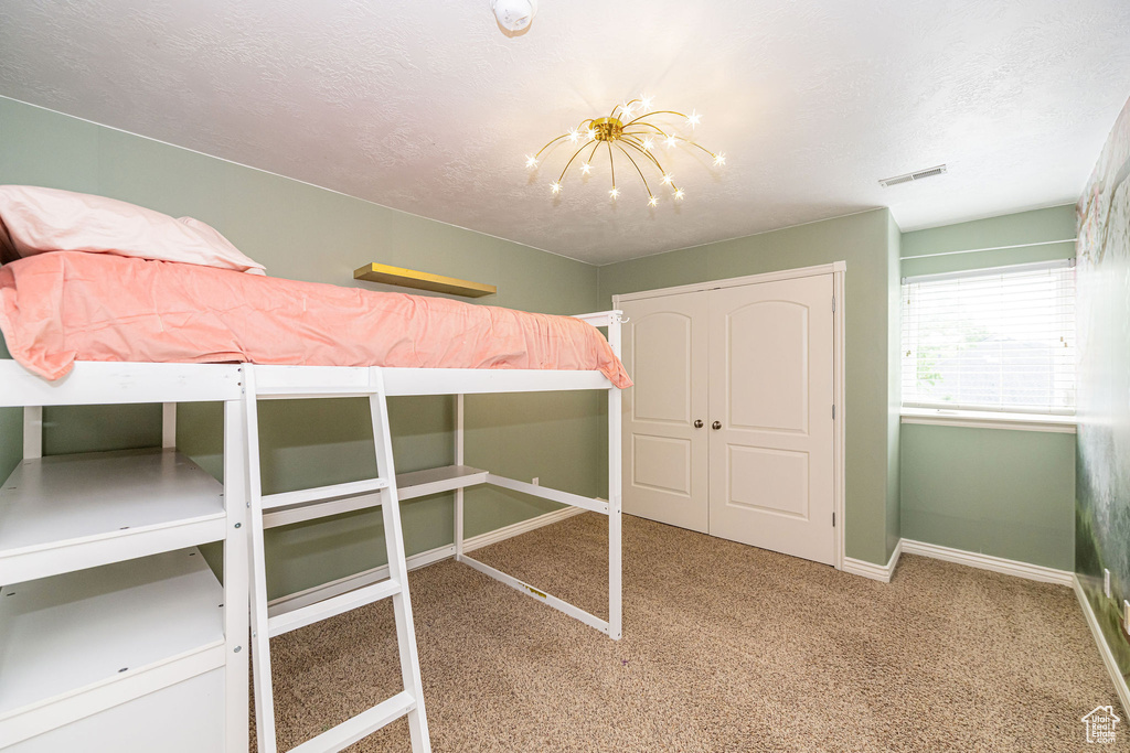 Unfurnished bedroom featuring carpet floors, baseboards, a chandelier, a textured ceiling, and a closet