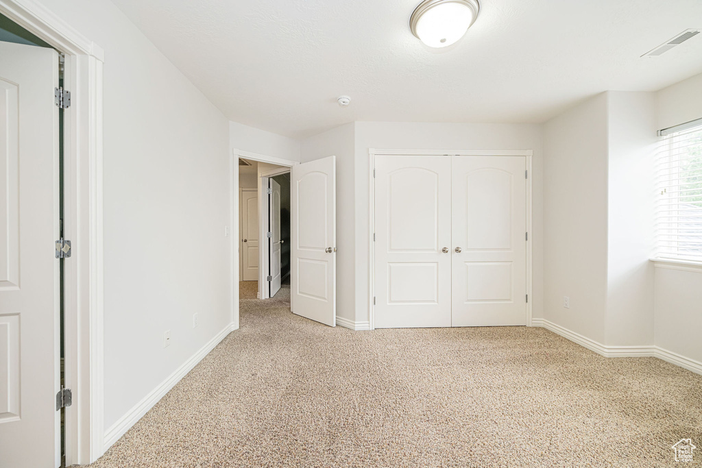 Unfurnished bedroom with light colored carpet, a closet, and baseboards