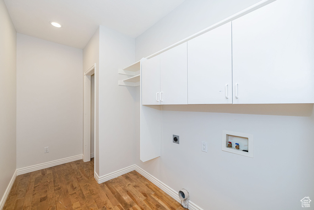 Washroom featuring hookup for an electric dryer, hookup for a washing machine, cabinet space, light wood finished floors, and baseboards