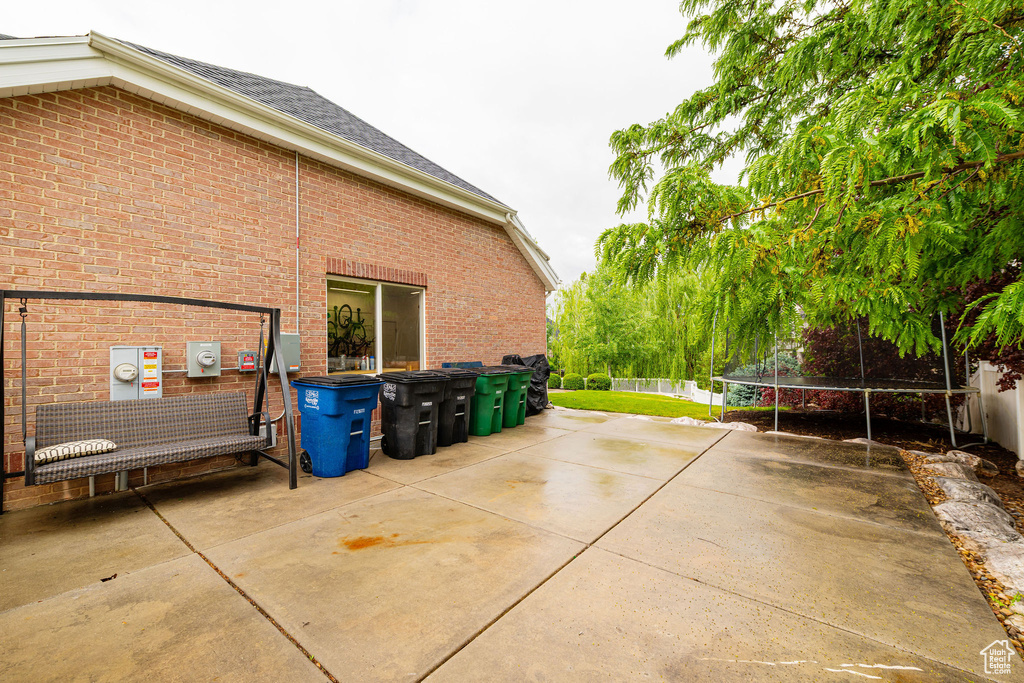 View of property exterior with a trampoline, brick siding, a patio, and fence