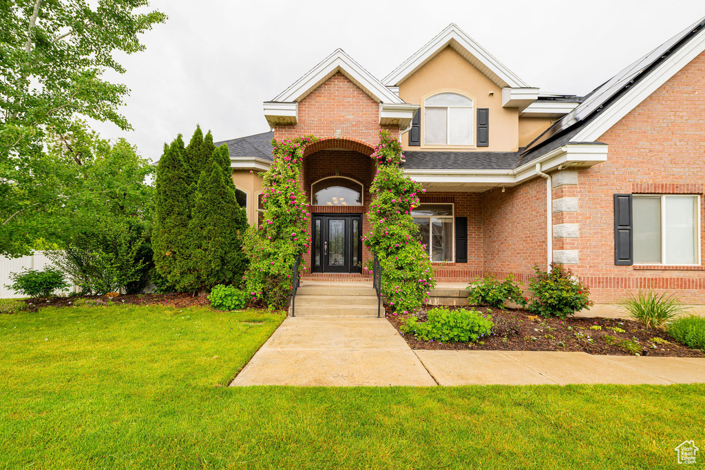 View of front of house featuring a front lawn, brick siding, a shingled roof, and stucco siding
