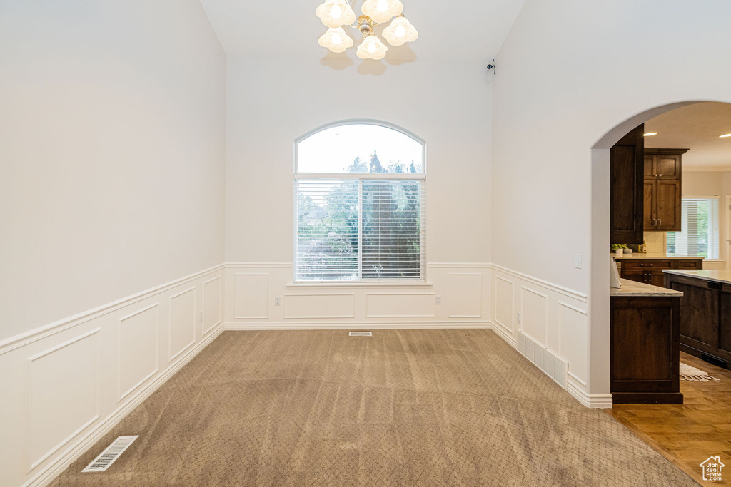 Unfurnished dining area with arched walkways, a chandelier, a decorative wall, wainscoting, and light colored carpet