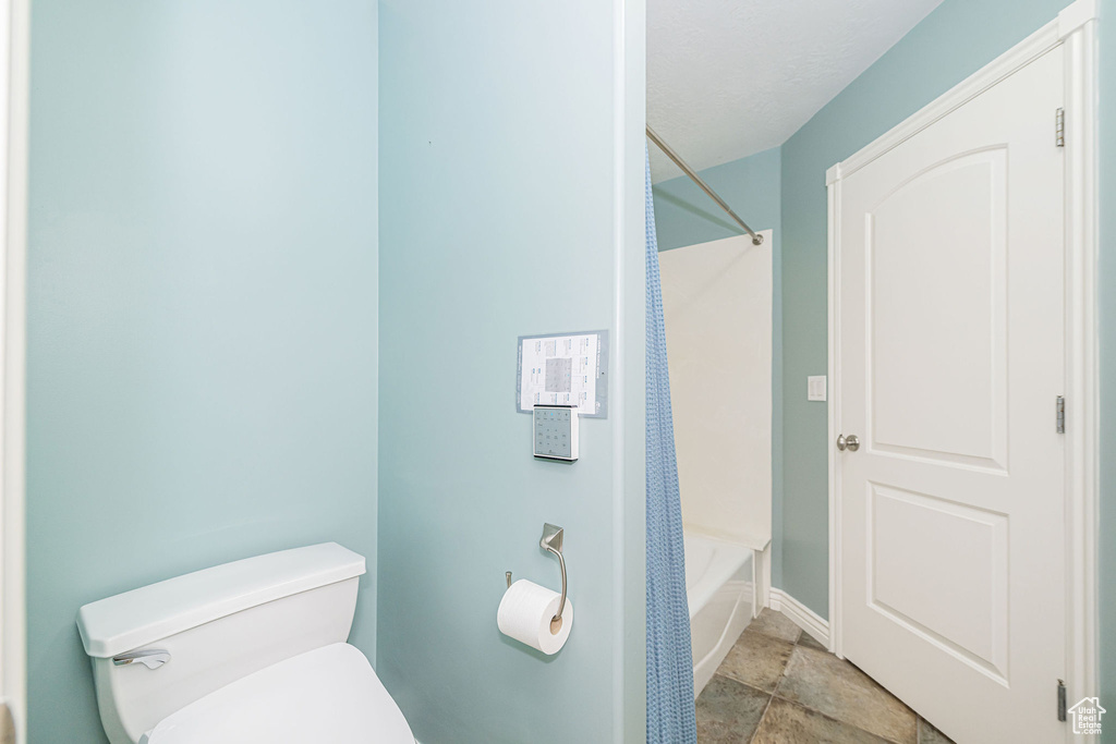 Bathroom with toilet, stone finish floors, tub / shower combination, and baseboards