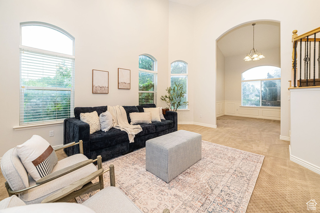 Living area with a chandelier, light carpet, a high ceiling, arched walkways, and a wainscoted wall
