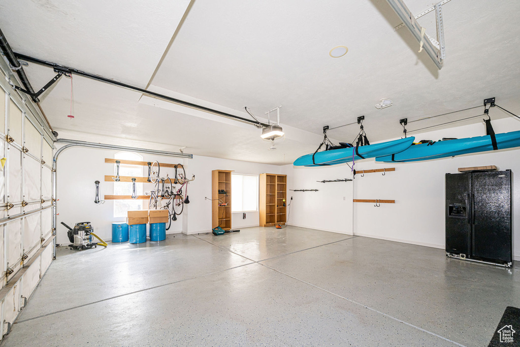 Garage featuring black fridge with ice dispenser and a garage door opener