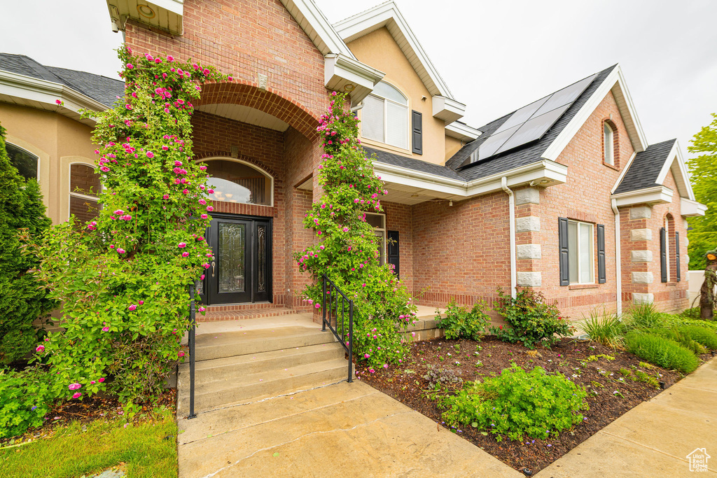 Property entrance featuring solar panels, brick siding, roof with shingles, and a porch