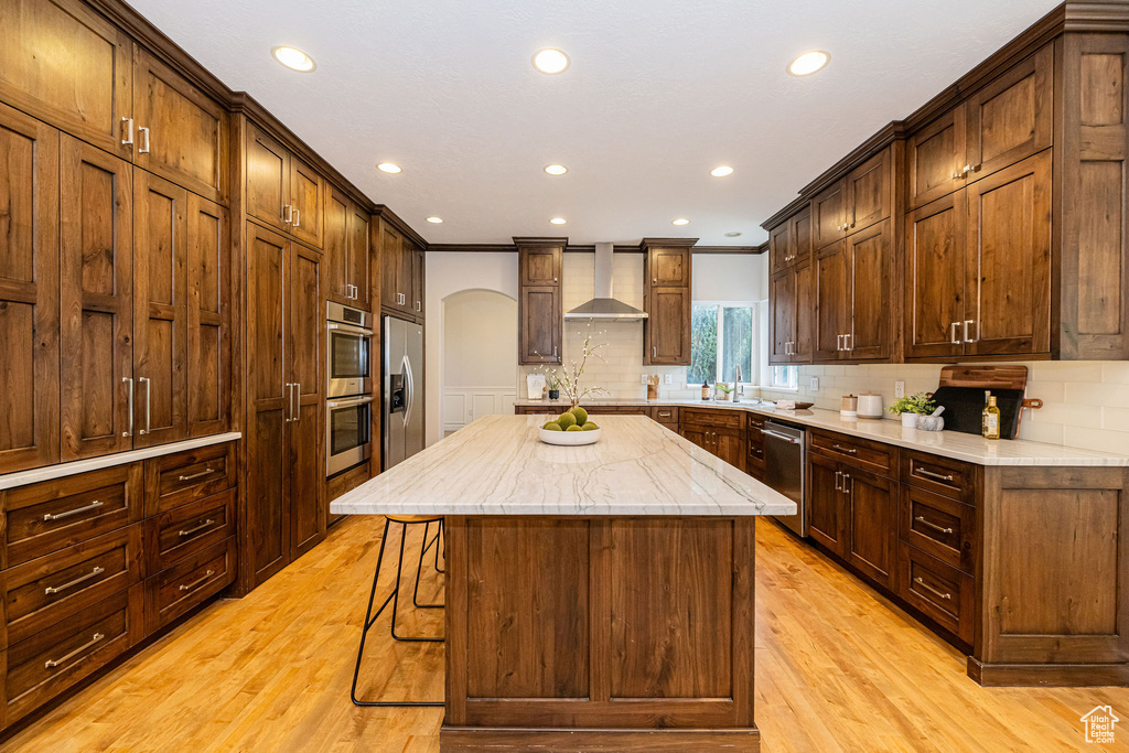Kitchen featuring wall chimney exhaust hood, arched walkways, stainless steel appliances, a sink, and a center island