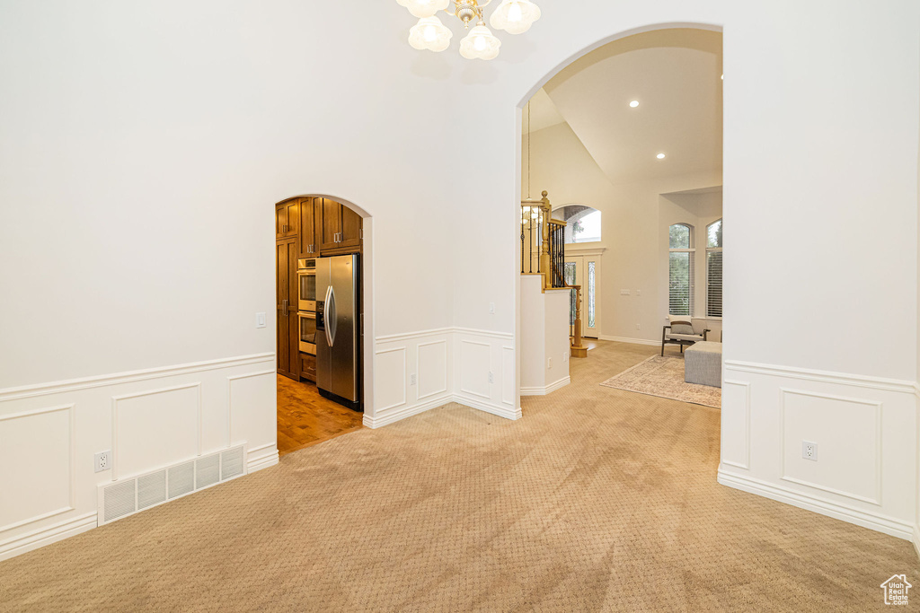 Unfurnished room featuring arched walkways, a chandelier, a decorative wall, light carpet, and wainscoting