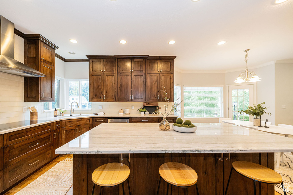 Kitchen with wall chimney range hood, a sink, ornamental molding, backsplash, and a large island