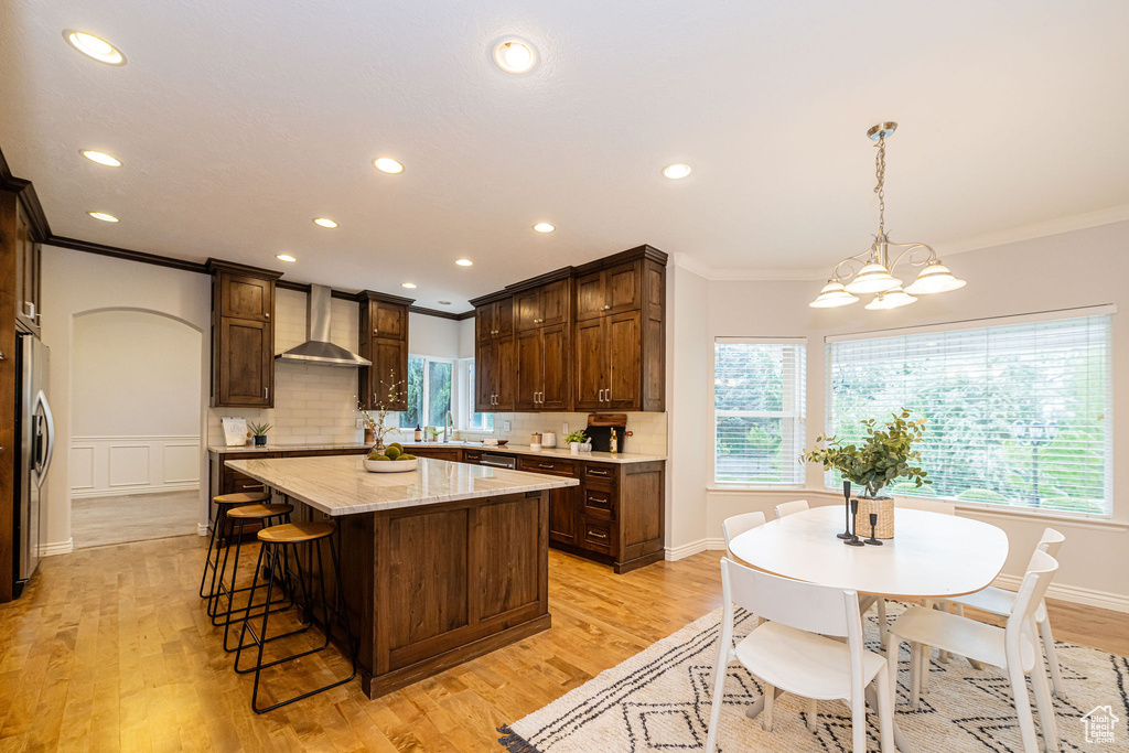 Kitchen featuring wall chimney exhaust hood, ornamental molding, freestanding refrigerator, a kitchen island, and recessed lighting