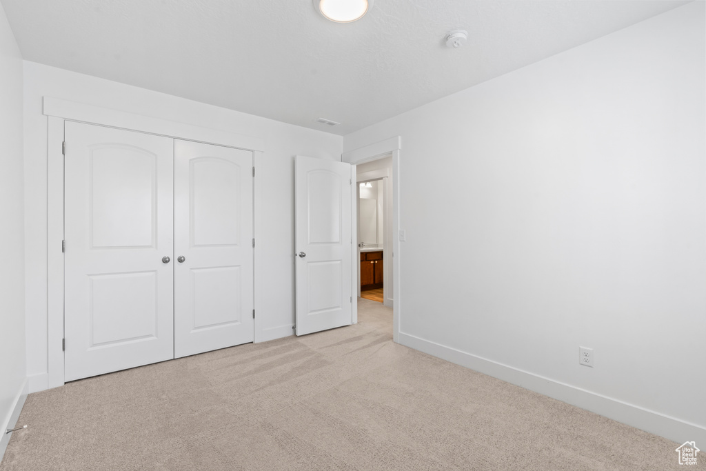 Unfurnished bedroom featuring light carpet, baseboards, and a closet