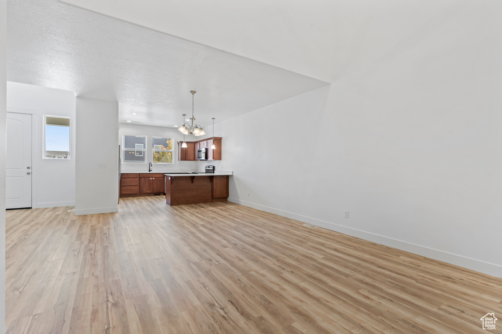 Unfurnished living room featuring a chandelier, baseboards, and light wood-style flooring