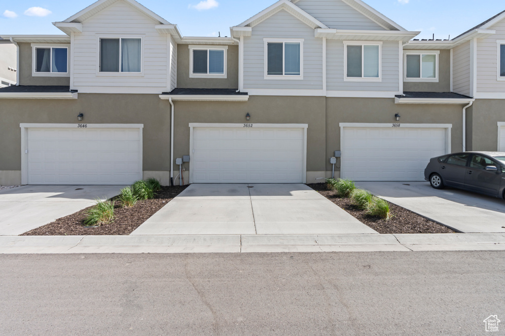 Townhome / multi-family property with an attached garage, stucco siding, and concrete driveway