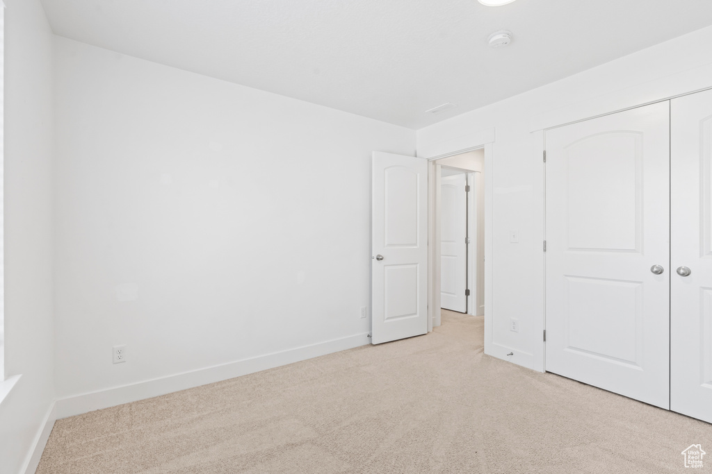 Unfurnished bedroom featuring light colored carpet, a closet, and baseboards