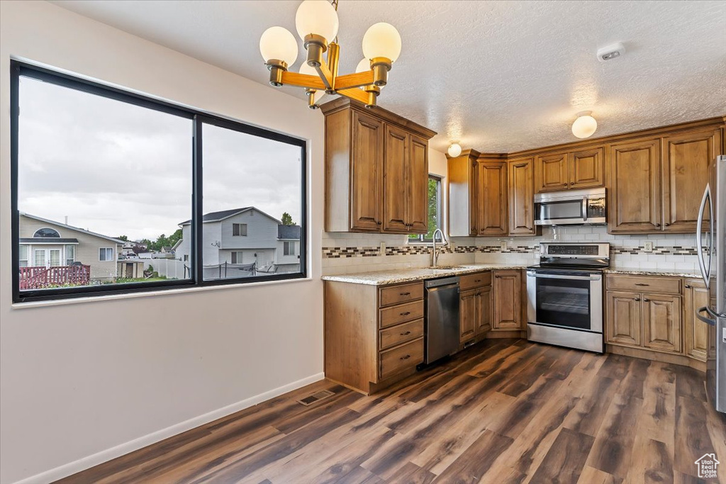 Kitchen featuring stainless steel appliances, a sink, a chandelier, tasteful backsplash, and a textured ceiling