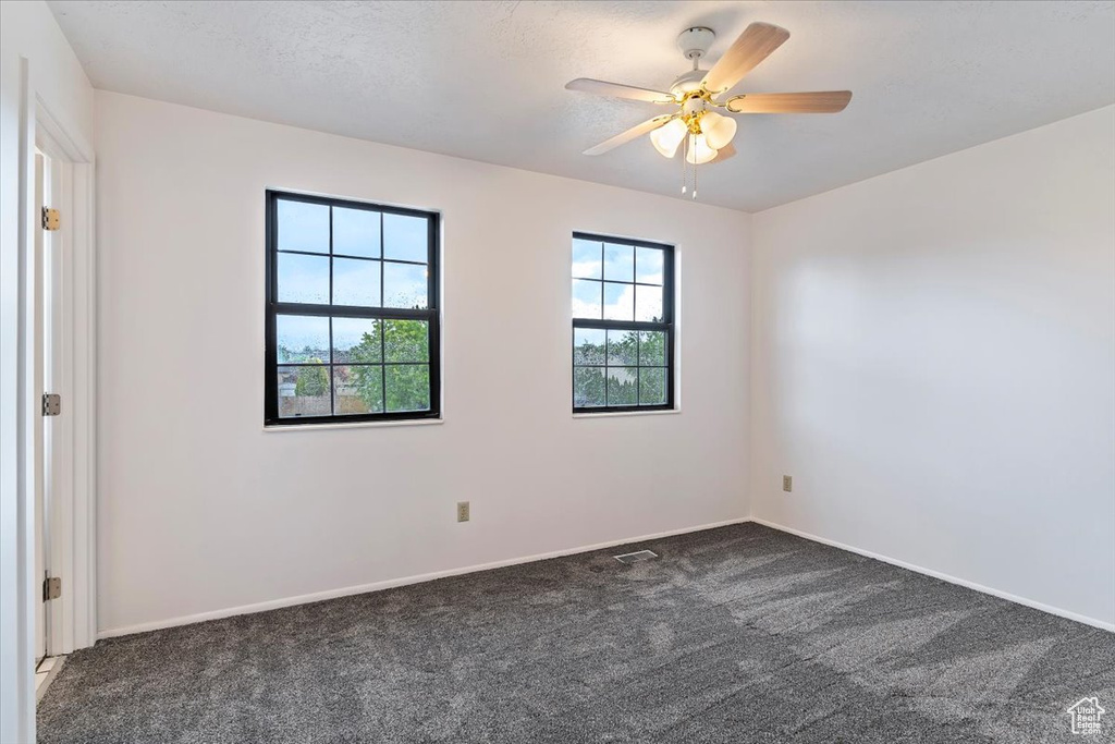 Unfurnished room with dark colored carpet, baseboards, and ceiling fan