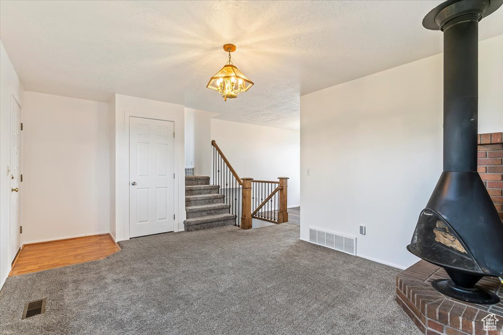 Unfurnished living room featuring a wood stove, carpet flooring, a chandelier, and stairs
