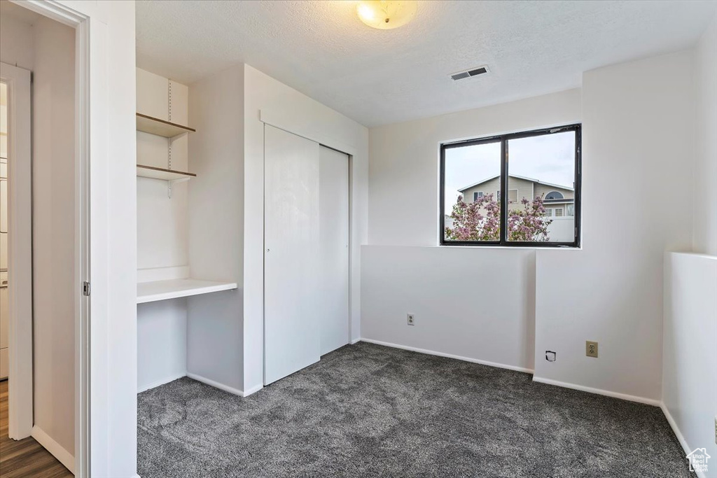Unfurnished bedroom with dark carpet, a closet, baseboards, and a textured ceiling