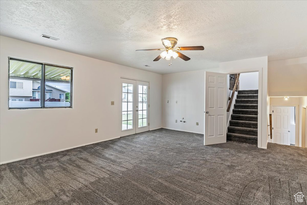 Unfurnished living room featuring french doors, dark colored carpet, stairs, ceiling fan, and a textured ceiling
