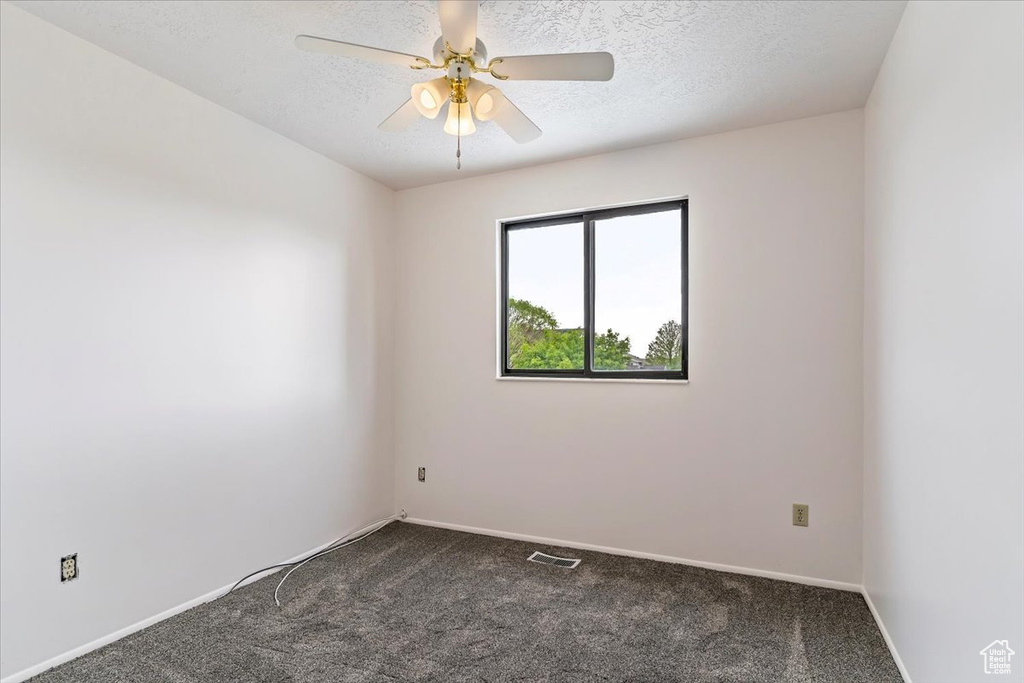 Empty room featuring dark carpet, a ceiling fan, baseboards, and a textured ceiling