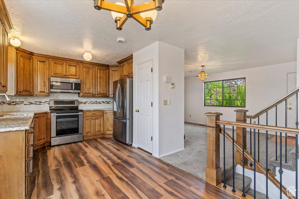Kitchen with stainless steel appliances, brown cabinetry, dark wood-style flooring, a textured ceiling, and backsplash