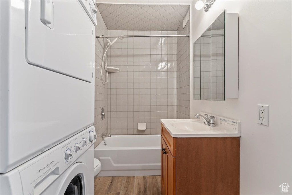 Bathroom with stacked washer / dryer, wood finished floors, shower / tub combination, vanity, and toilet