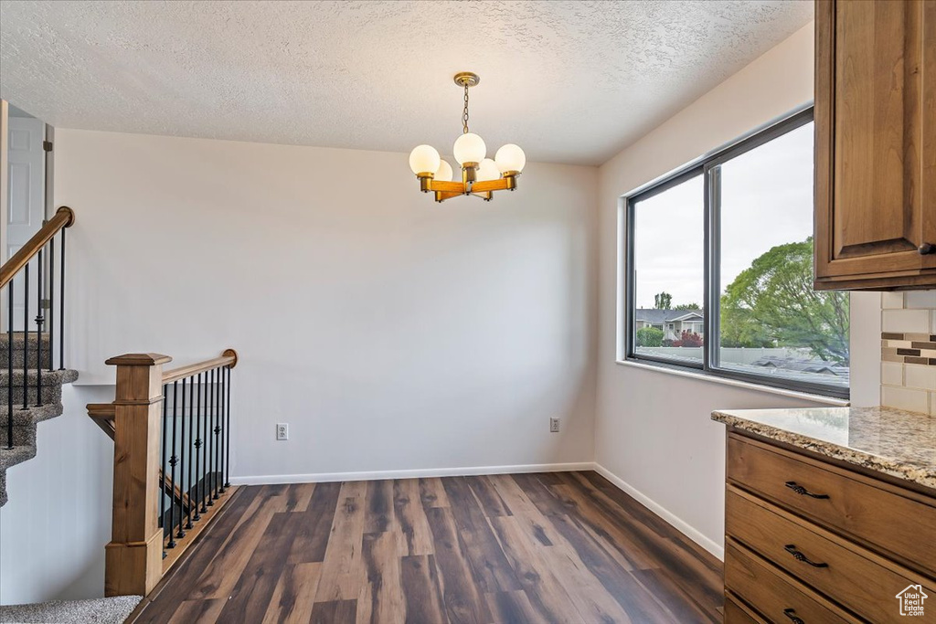 Unfurnished dining area with a chandelier, dark wood-type flooring, a textured ceiling, baseboards, and stairs