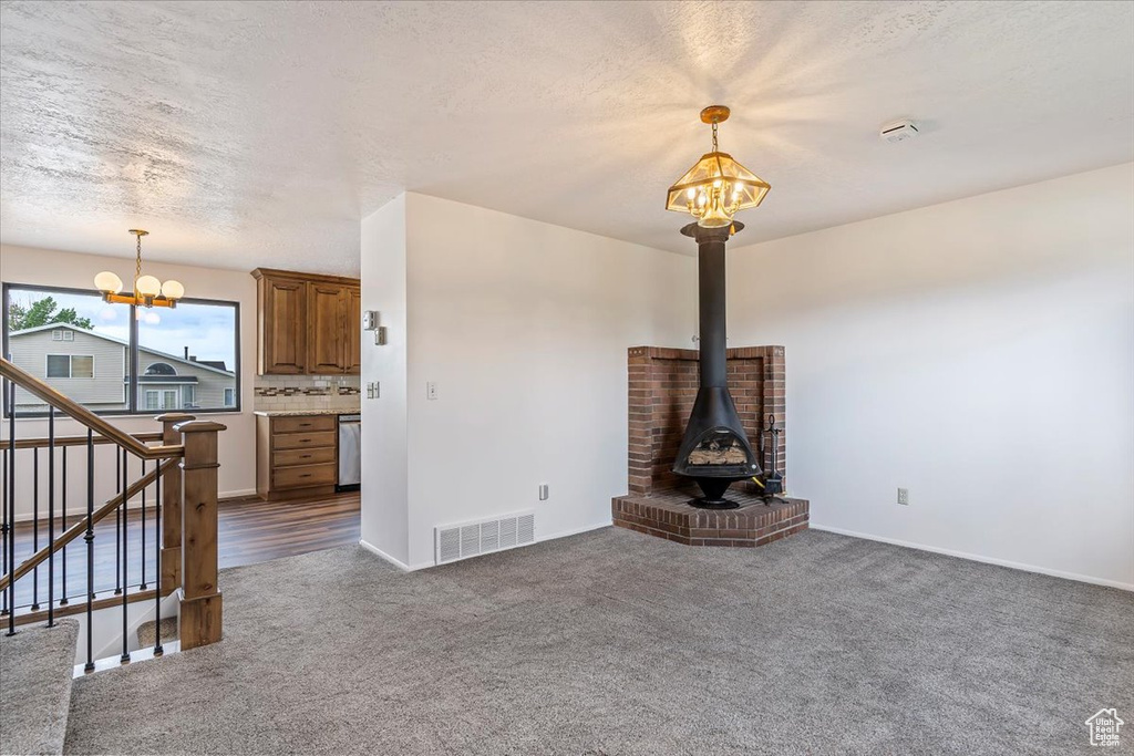 Unfurnished living room featuring a chandelier, dark carpet, stairs, baseboards, and a textured ceiling