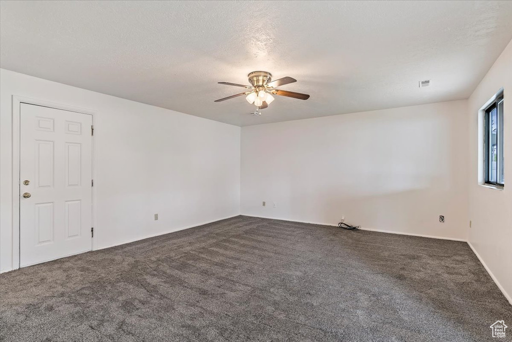 Empty room featuring ceiling fan and dark carpet