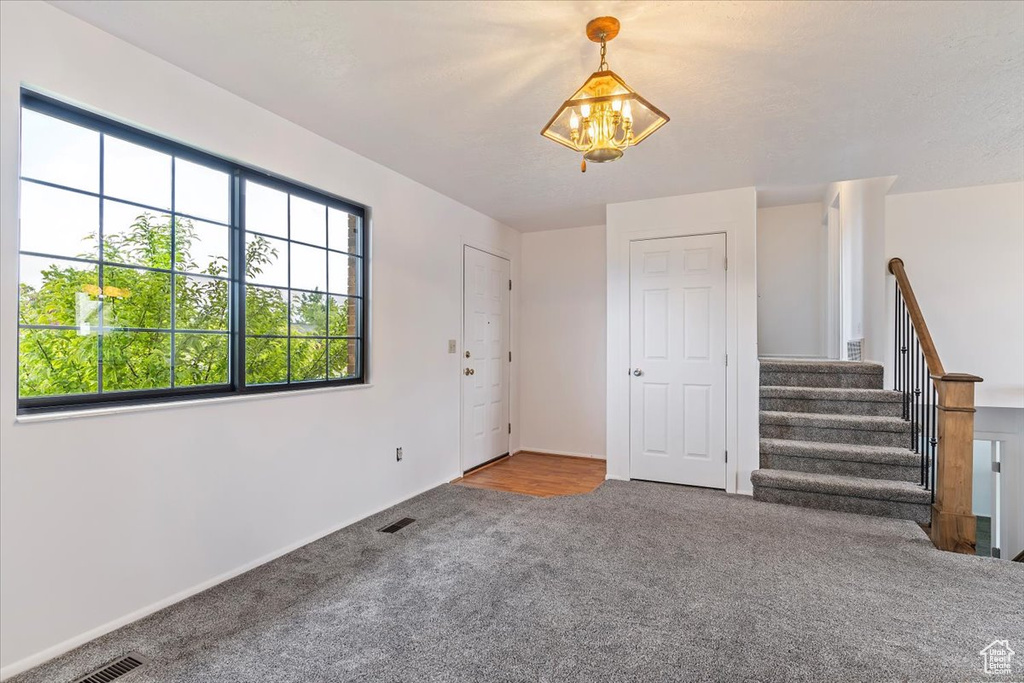 Unfurnished living room with a chandelier, carpet flooring, stairway, and baseboards