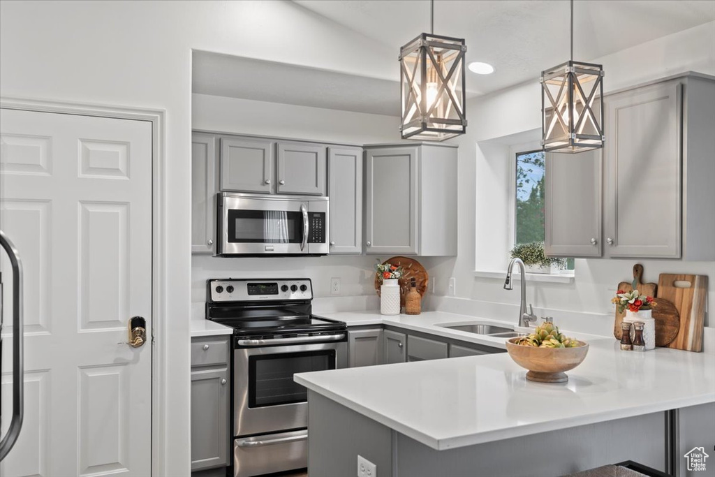 Kitchen with appliances with stainless steel finishes, gray cabinets, a sink, a peninsula, and light countertops