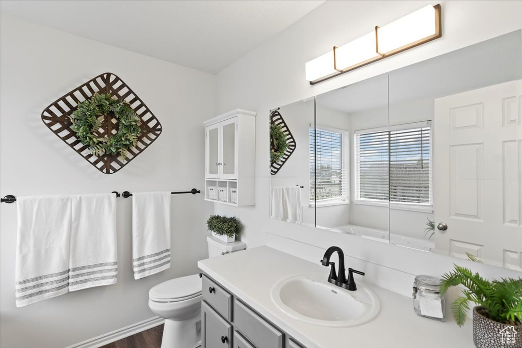 Full bath with vanity, toilet, wood finished floors, and a tub to relax in