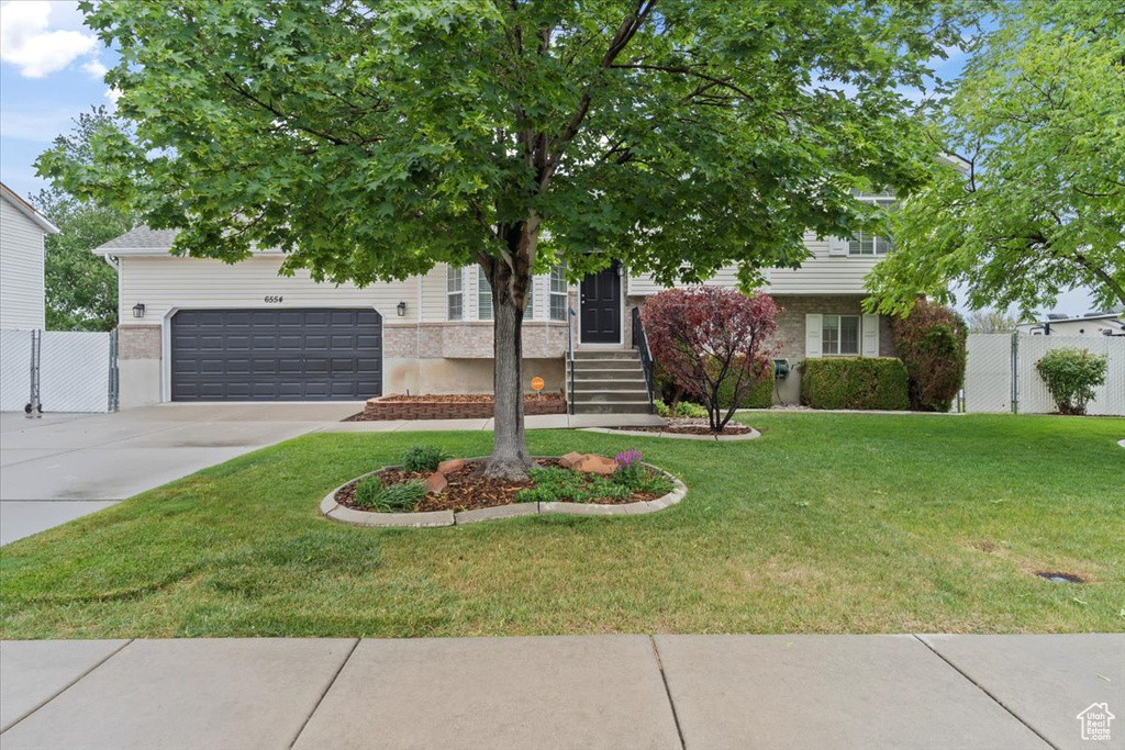 View of property hidden behind natural elements featuring concrete driveway, brick siding, and a gate