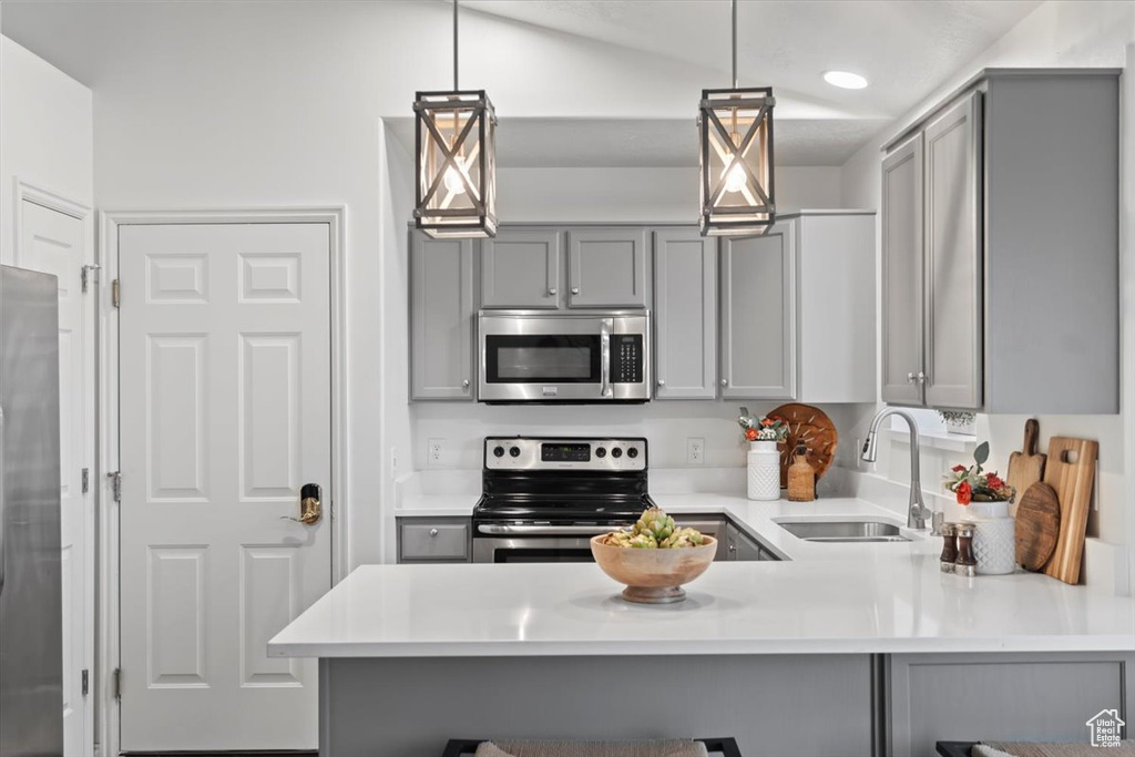 Kitchen with stainless steel appliances, gray cabinetry, a sink, a peninsula, and light countertops