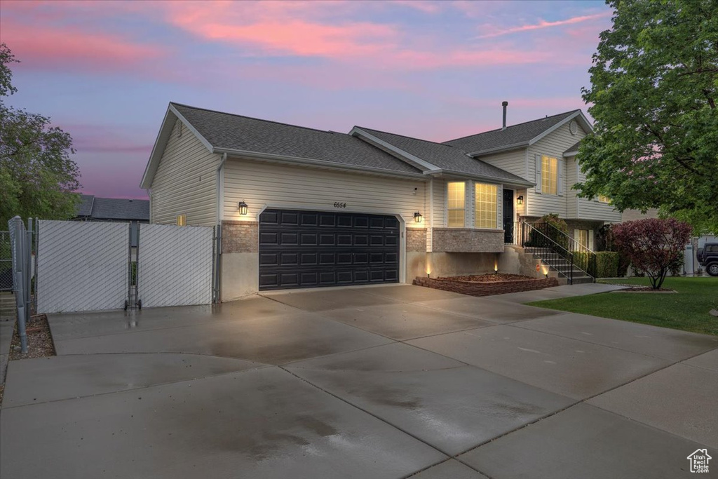 Tri-level home featuring an attached garage, driveway, a gate, a shingled roof, and brick siding