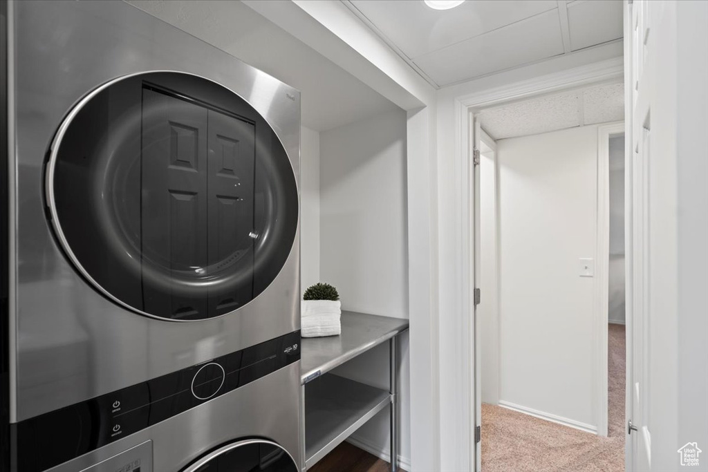 Clothes washing area featuring stacked washer and clothes dryer, carpet floors, and baseboards