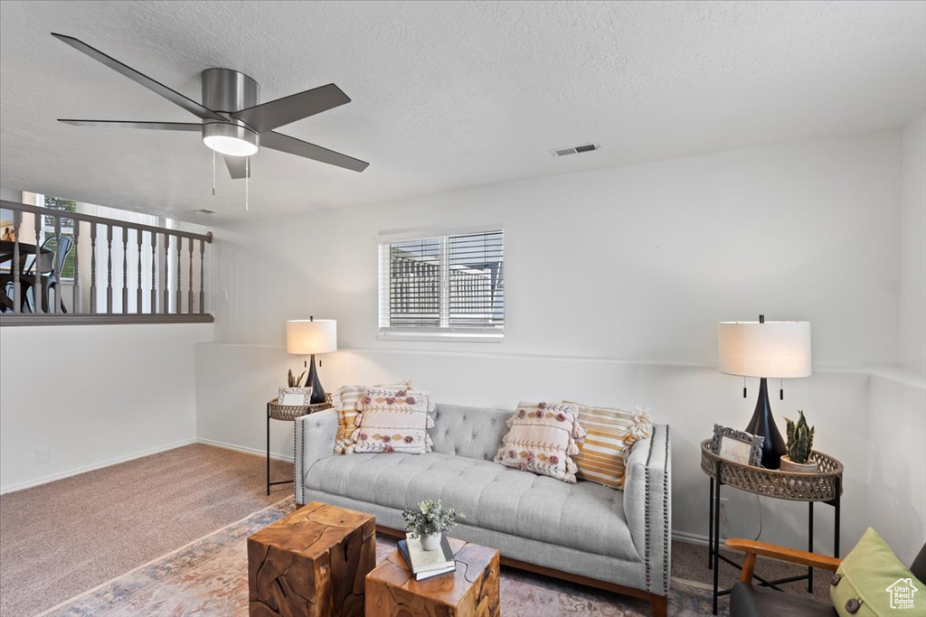 Carpeted living area with ceiling fan, a textured ceiling, and baseboards