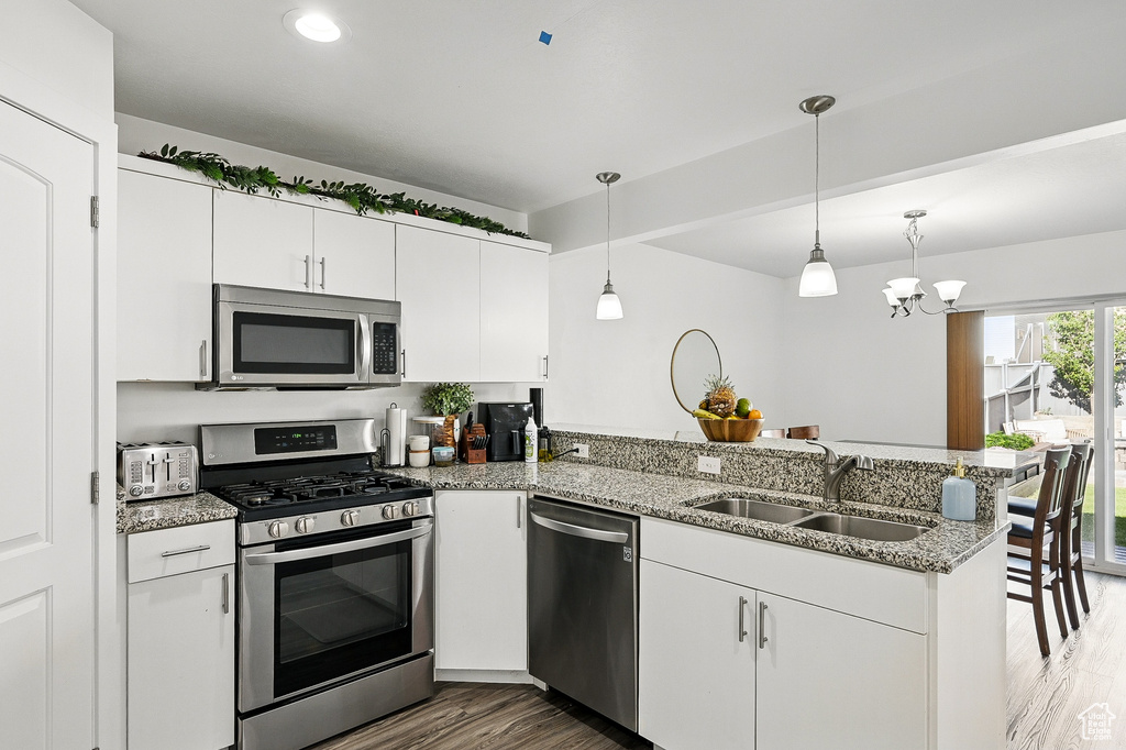 Kitchen with appliances with stainless steel finishes, a sink, a peninsula, wood finished floors, and white cabinetry