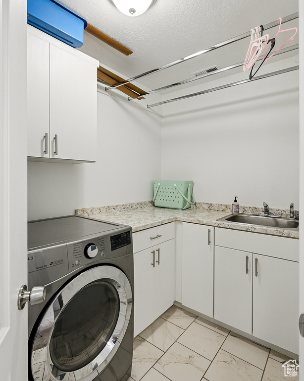Clothes washing area featuring washer / dryer, cabinet space, light marble finish flooring, and a textured ceiling
