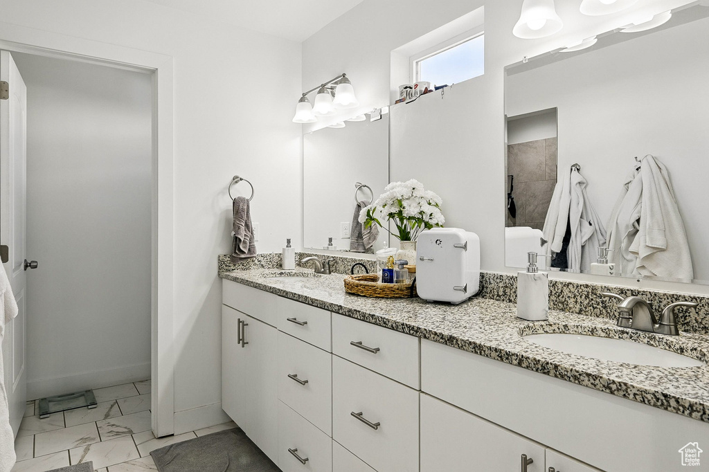 Bathroom featuring marble look tile flooring, double vanity, baseboards, and a tile shower
