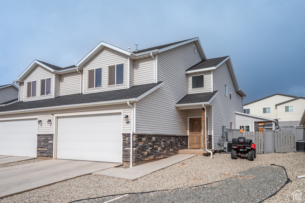 View of front facade featuring stone siding, an attached garage, driveway, and cooling unit
