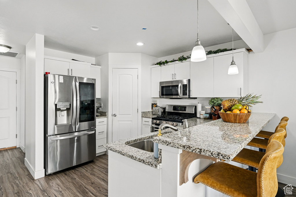 Kitchen with appliances with stainless steel finishes, a peninsula, a sink, decorative light fixtures, and dark wood-type flooring