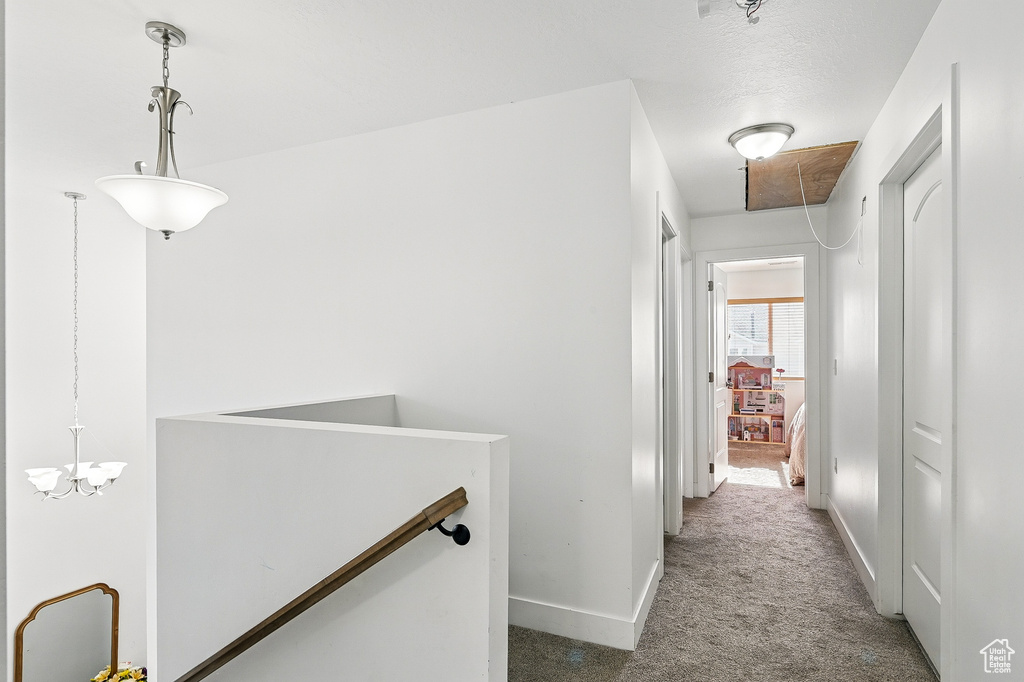 Hallway featuring carpet flooring, an upstairs landing, baseboards, and a chandelier