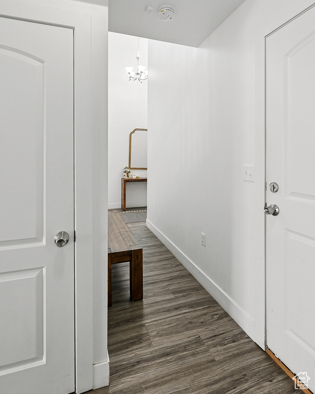 Hall featuring dark wood-style floors, baseboards, and a chandelier