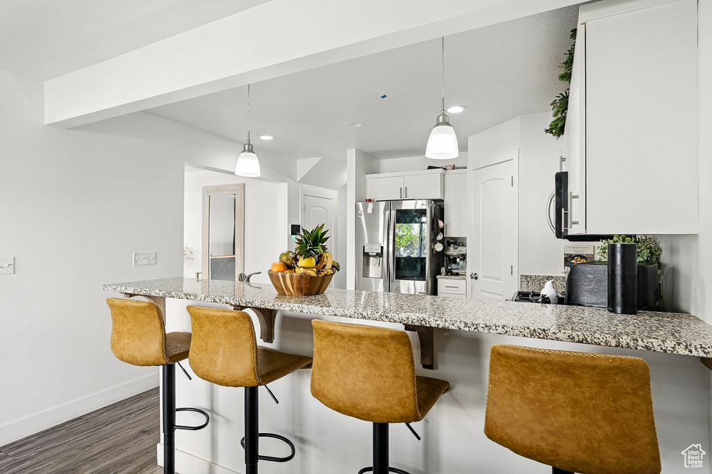Kitchen featuring appliances with stainless steel finishes, dark wood-style flooring, light stone countertops, baseboards, and a peninsula