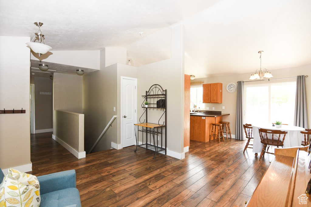 Living area featuring lofted ceiling, dark wood-type flooring, a chandelier, and baseboards