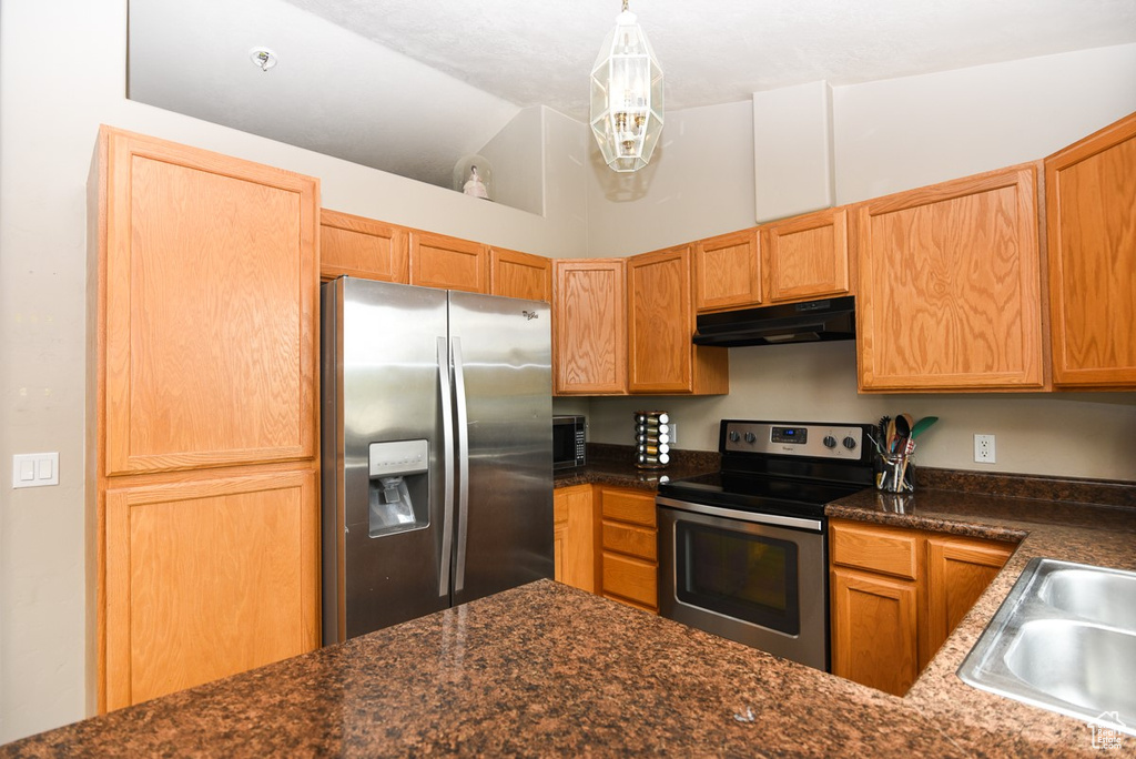 Kitchen with appliances with stainless steel finishes, under cabinet range hood, dark countertops, a sink, and lofted ceiling