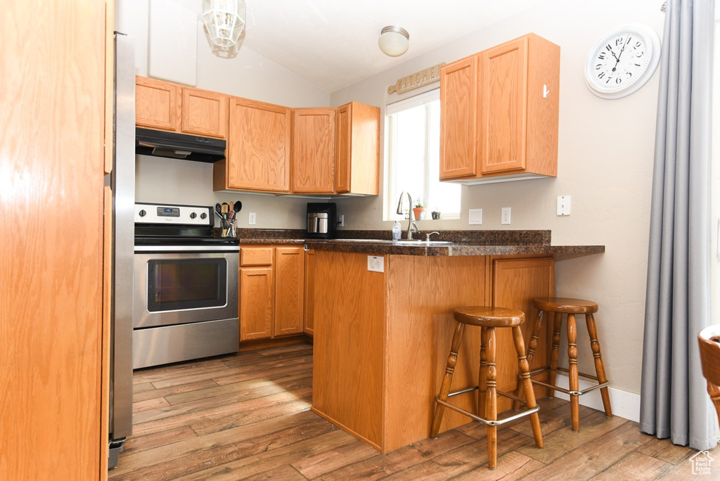 Kitchen featuring stainless steel electric range, under cabinet range hood, vaulted ceiling, light wood-style floors, and dark countertops