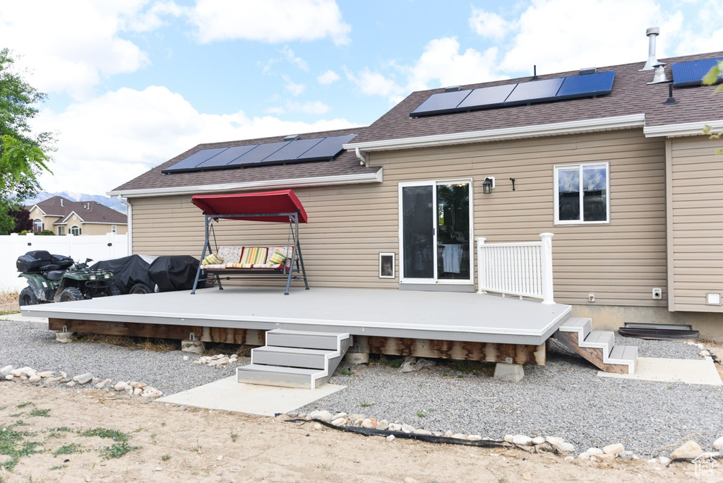 Back of property featuring roof mounted solar panels, a shingled roof, a deck, and fence